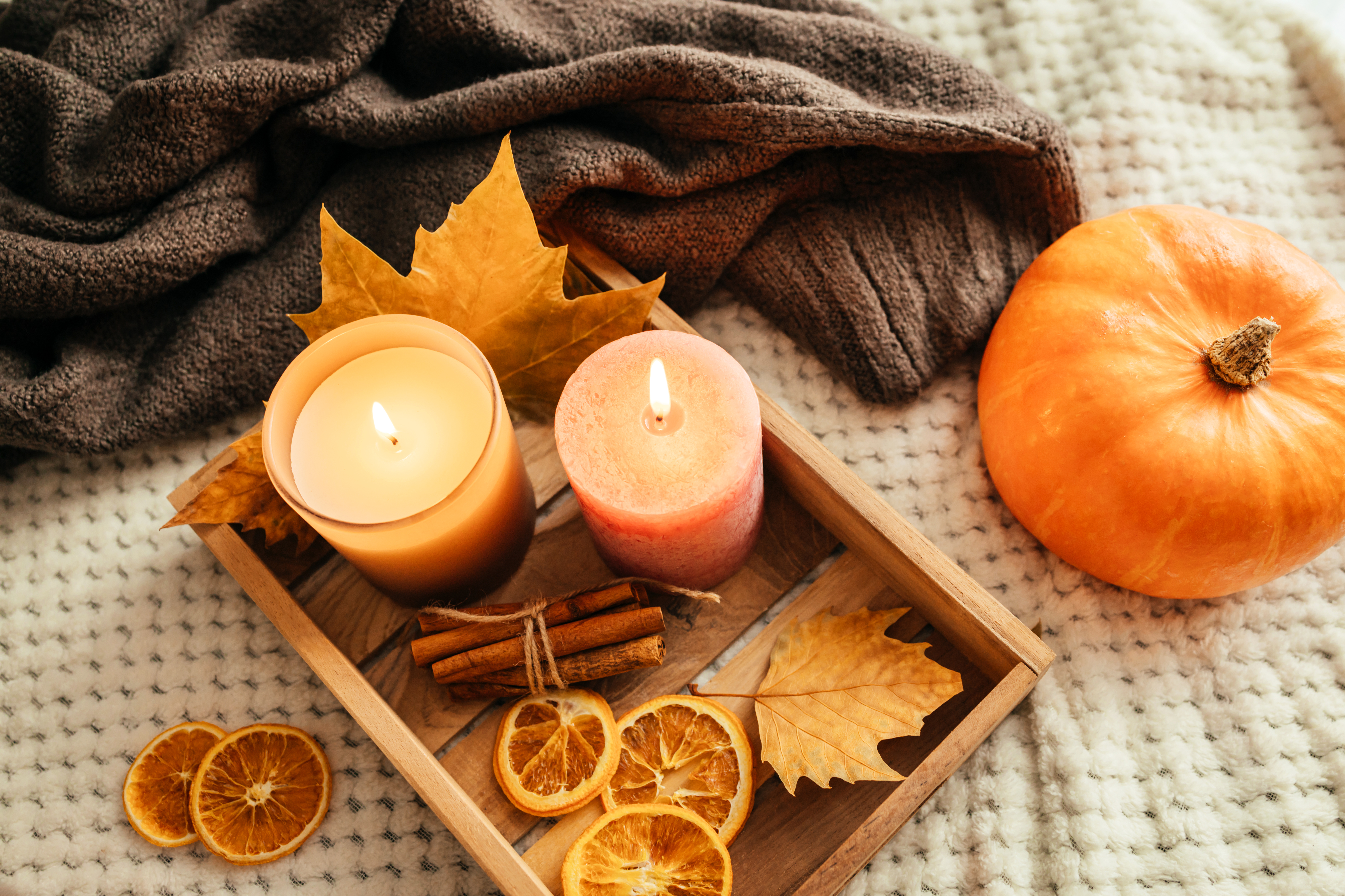 composition of a knitted sweater and autumn home decor. Candles, fallen leaves, pumpkin and cinnamon